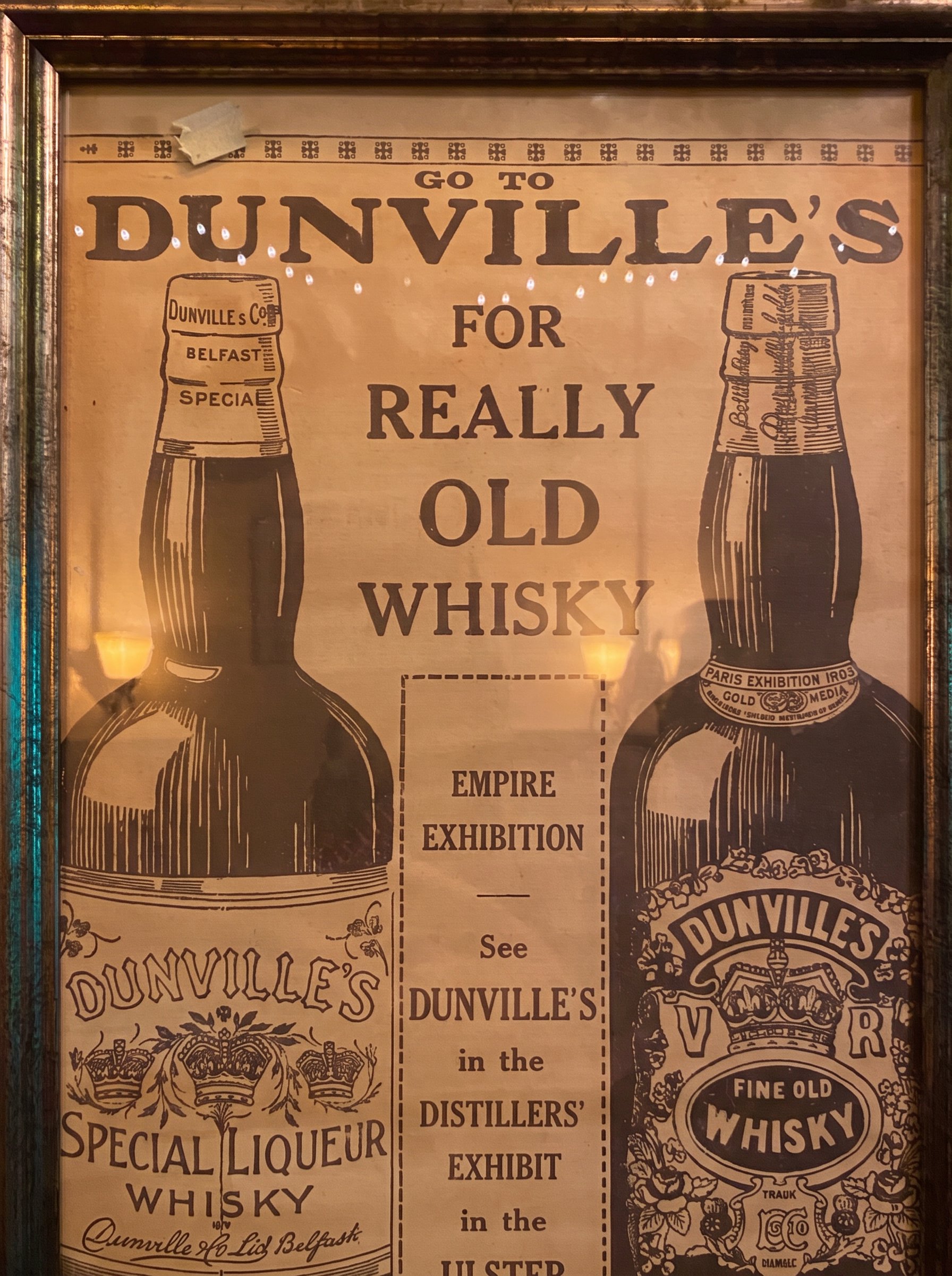 A vintage Dunville's whiskey advertisement framed on brick