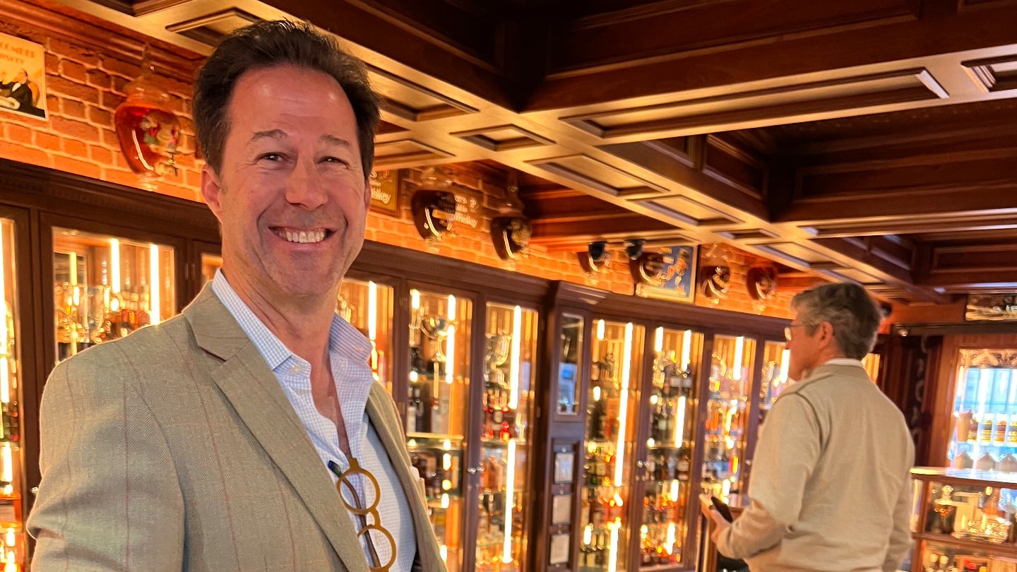 Michael Sloan smiling before lit cabinets of rare Irish whiskey