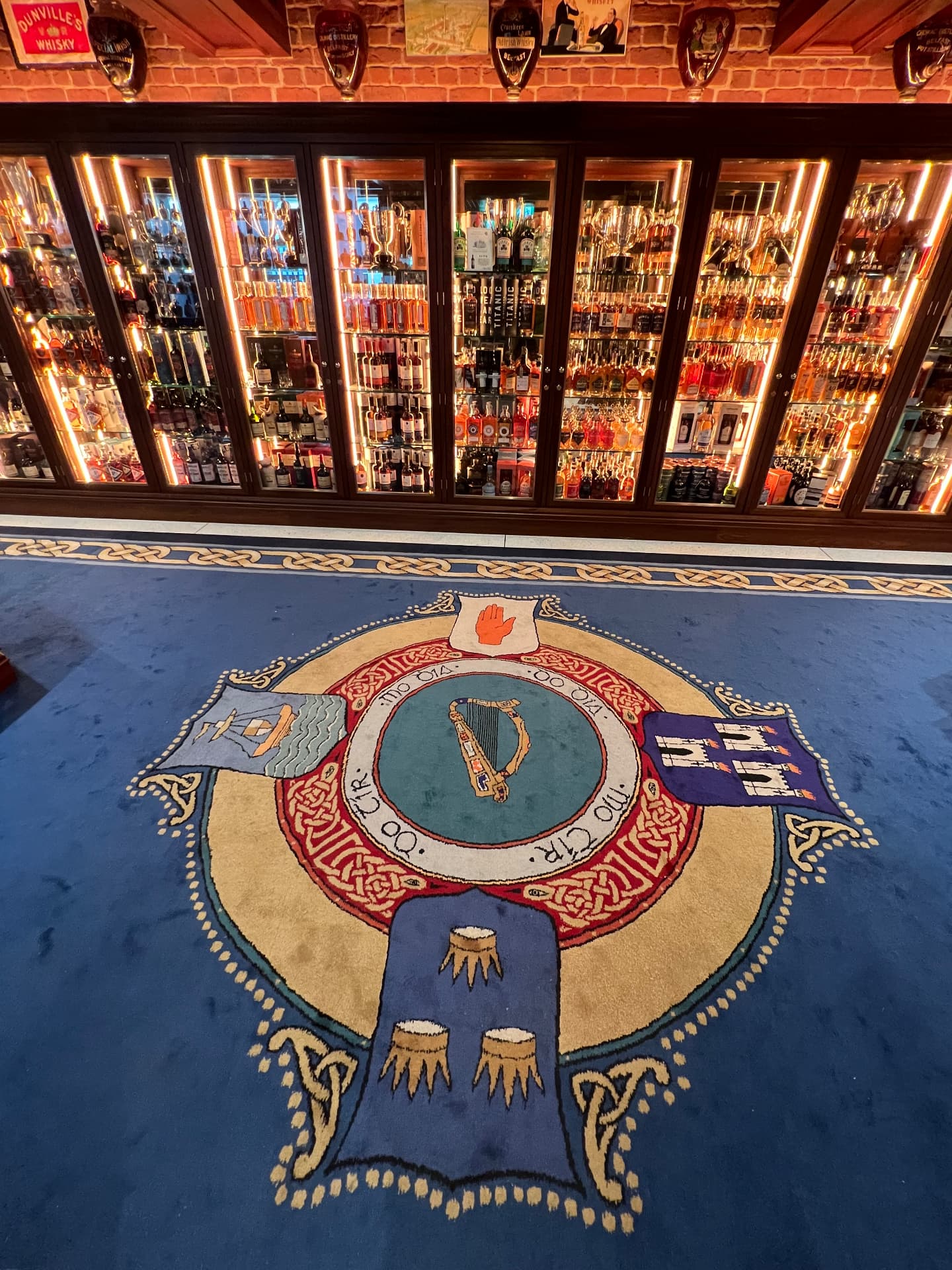 An Irish heraldic crest woven into the carpet before lit whiskey cabinets