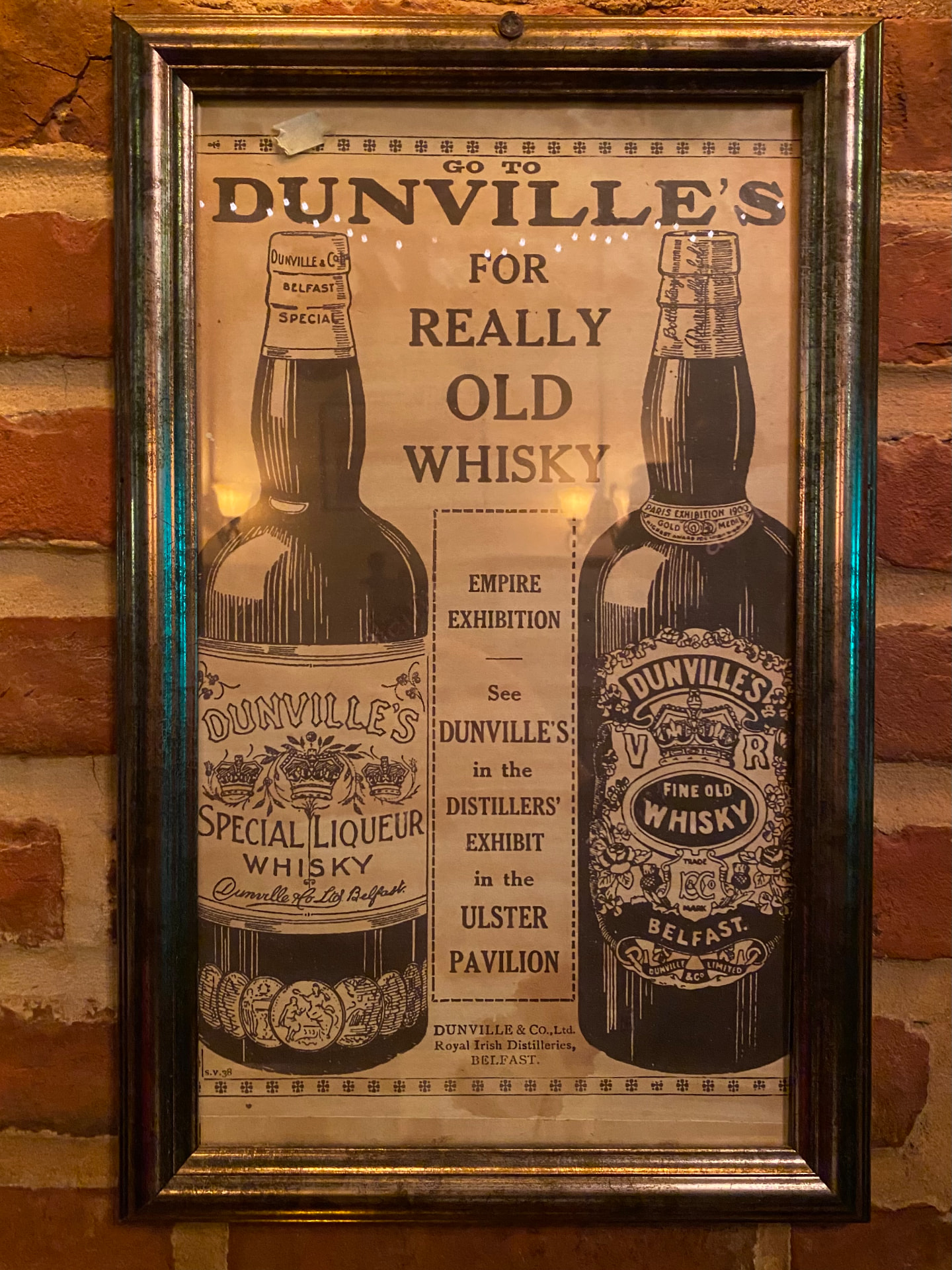 A vintage Dunville's whiskey advertisement framed on brick